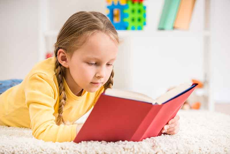 a caucasian child in a yellow sweater reading a book