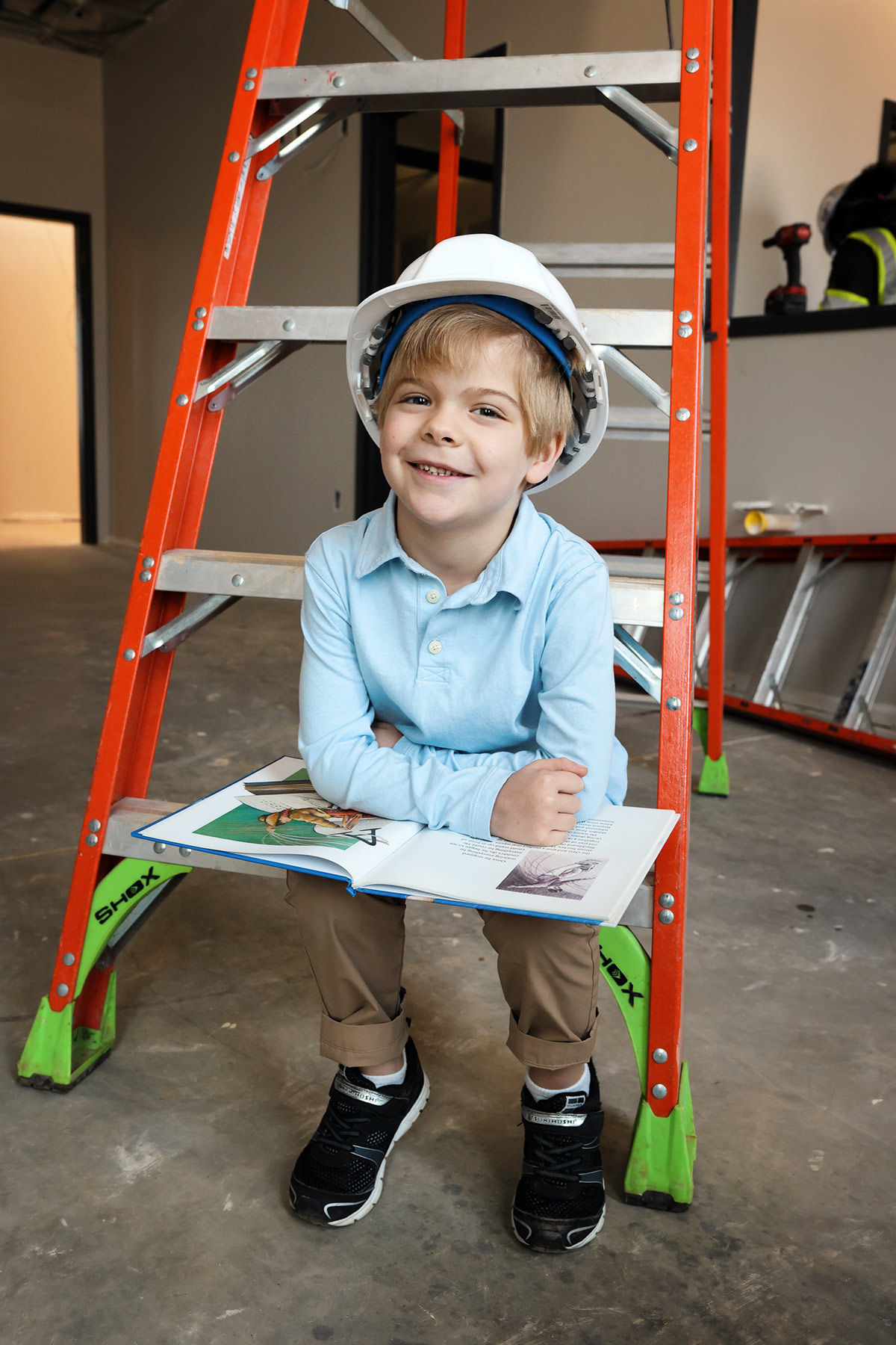 Child holding a book, sitting on a ladder.