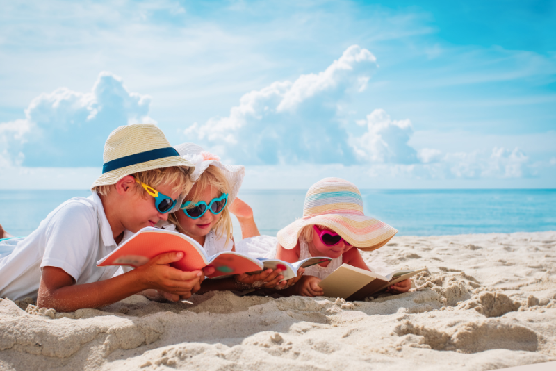 3 kids read on a beach