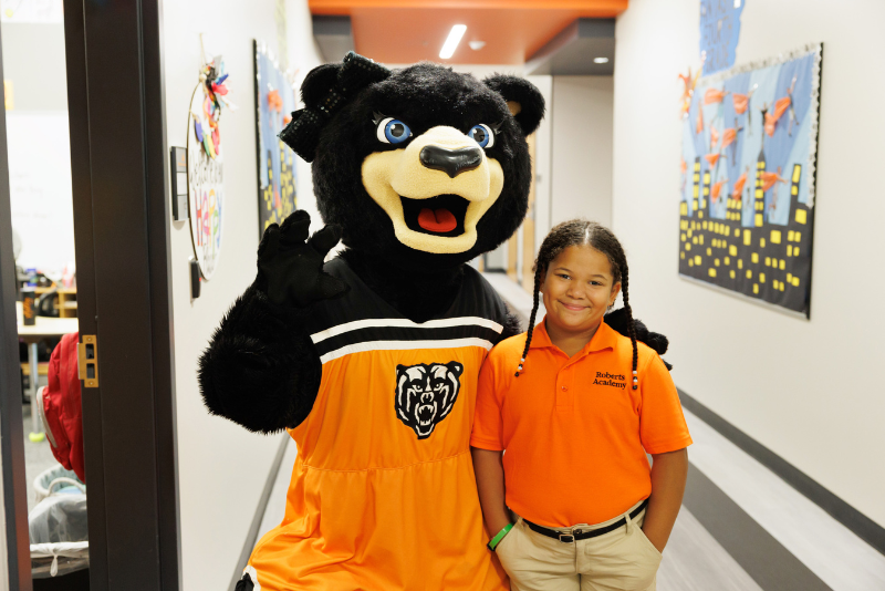 A Roberts Academy at Mercer University student poses with a Tot, a Mercer University mascot bear.