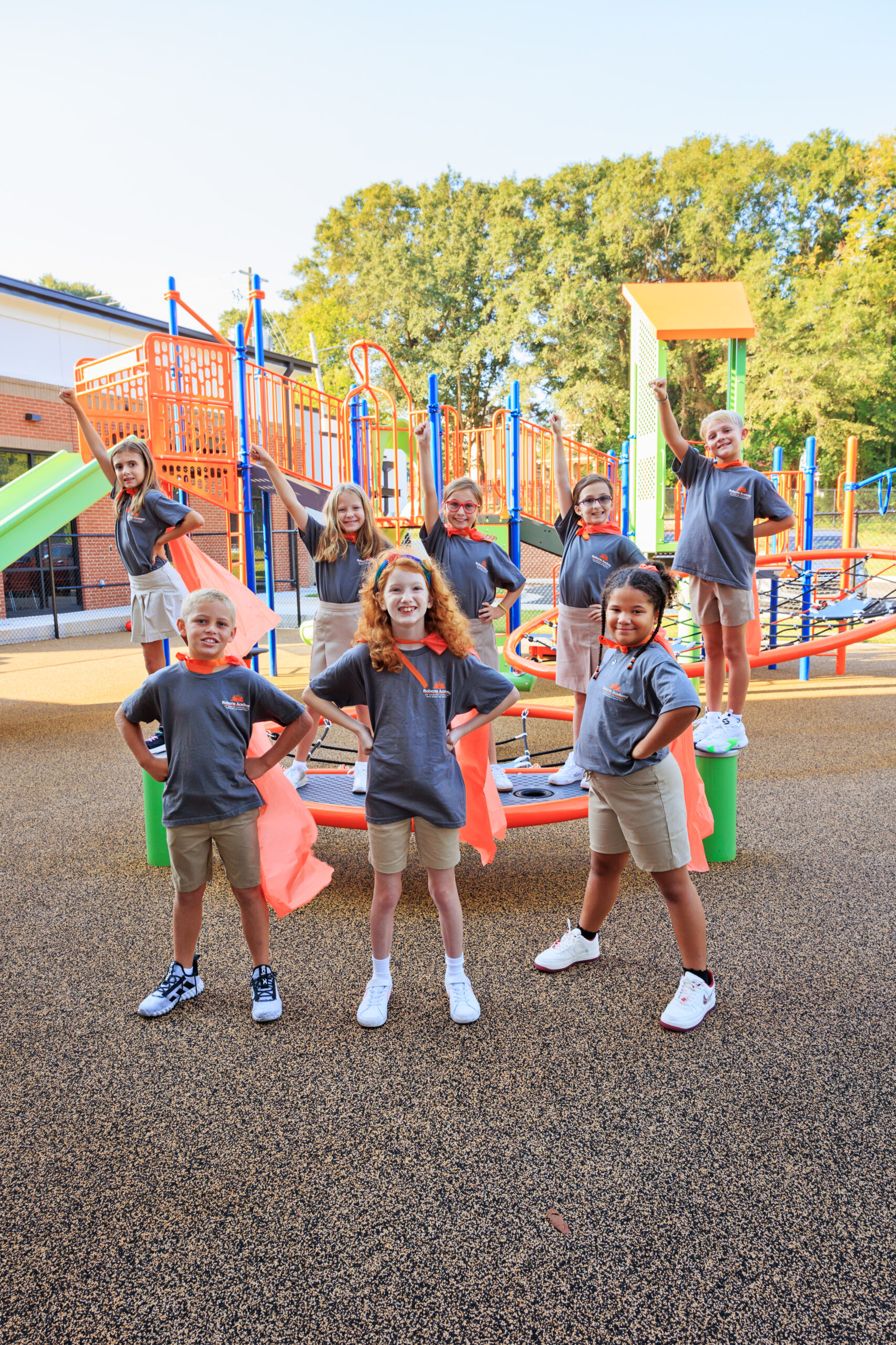 A group of students wear capes and pose like super heroes on the Roberts Academy at Mercer University playground