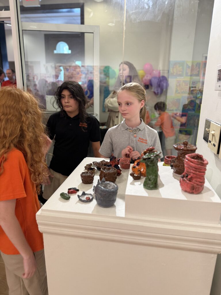 Roberts Academy at Mercer University students gather around the ceramics display at the first student art show. 