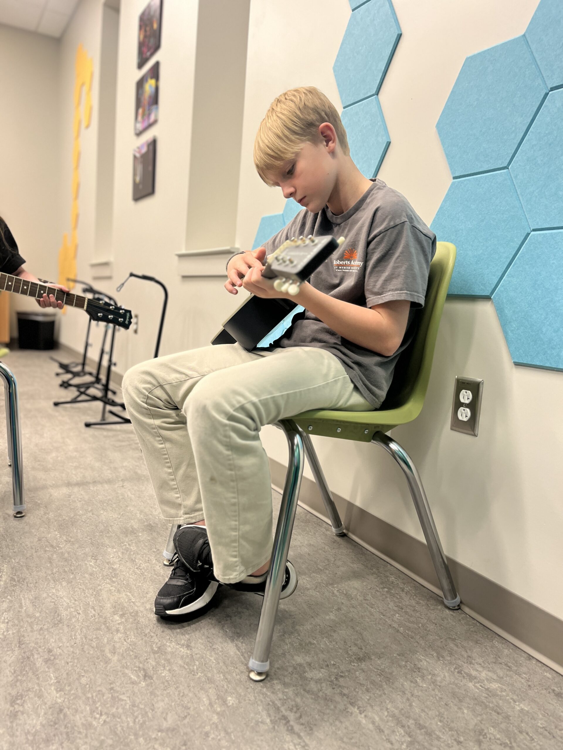 A Roberts Academy student in a gray Roberts Academy t-shirt practices the guitar