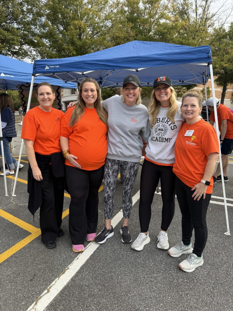 Roberts Academy at Mercer University faculty and staff, wearing Roberts Academy t-shirts and sweatshirts, pose together in front of a blue tent at the 2025 Dyslexia Dash in Atlanta, Georgia. 
