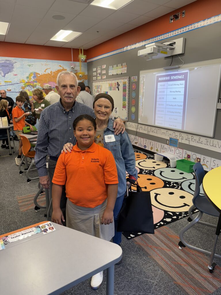 A Roberts Academy student poses with her grandparents in a classroom during the Academy's Grand Gathering Event. 