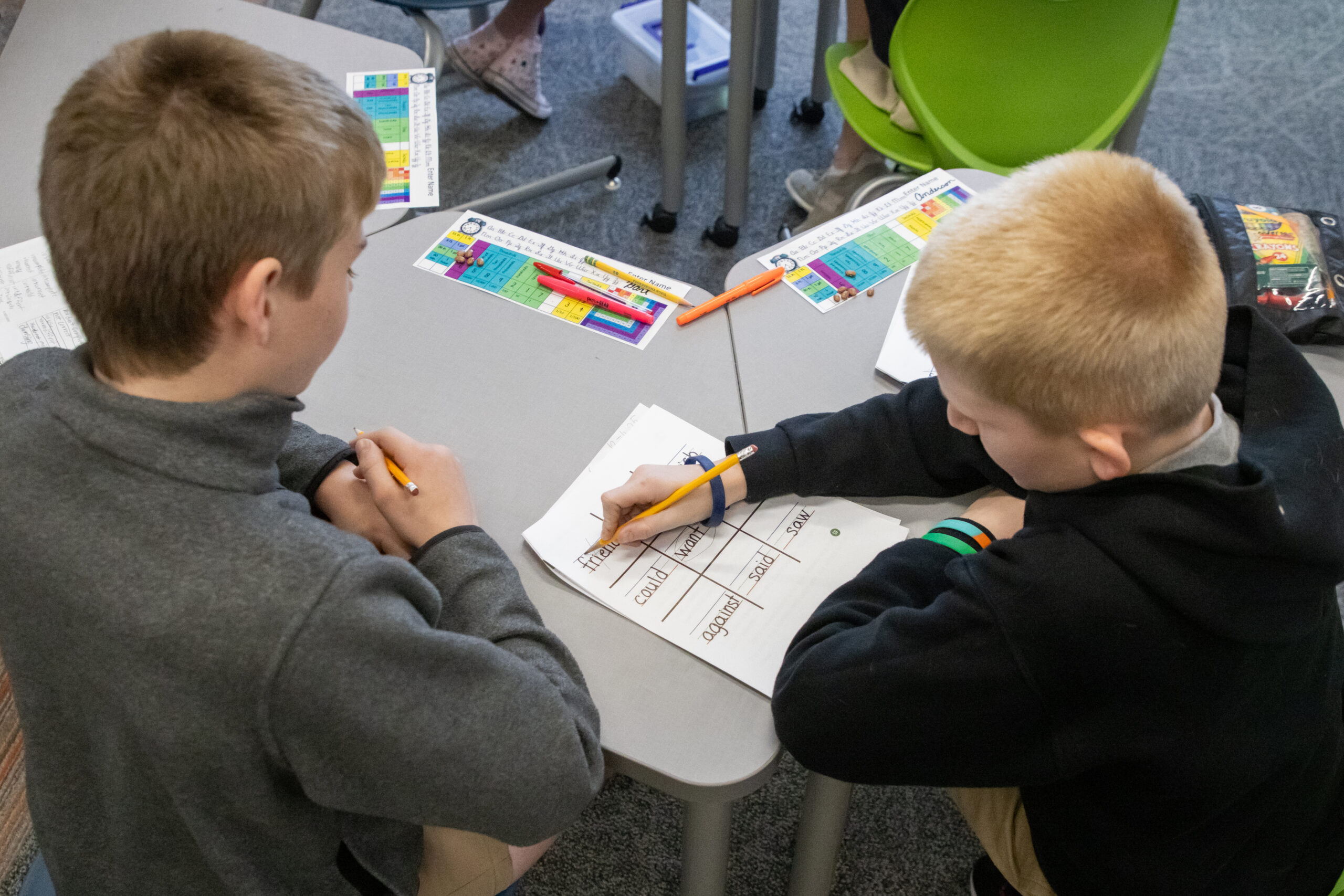 Two Roberts Academy at Mercer University students sitting at a gray desk work together to complete a phonics worksheet.