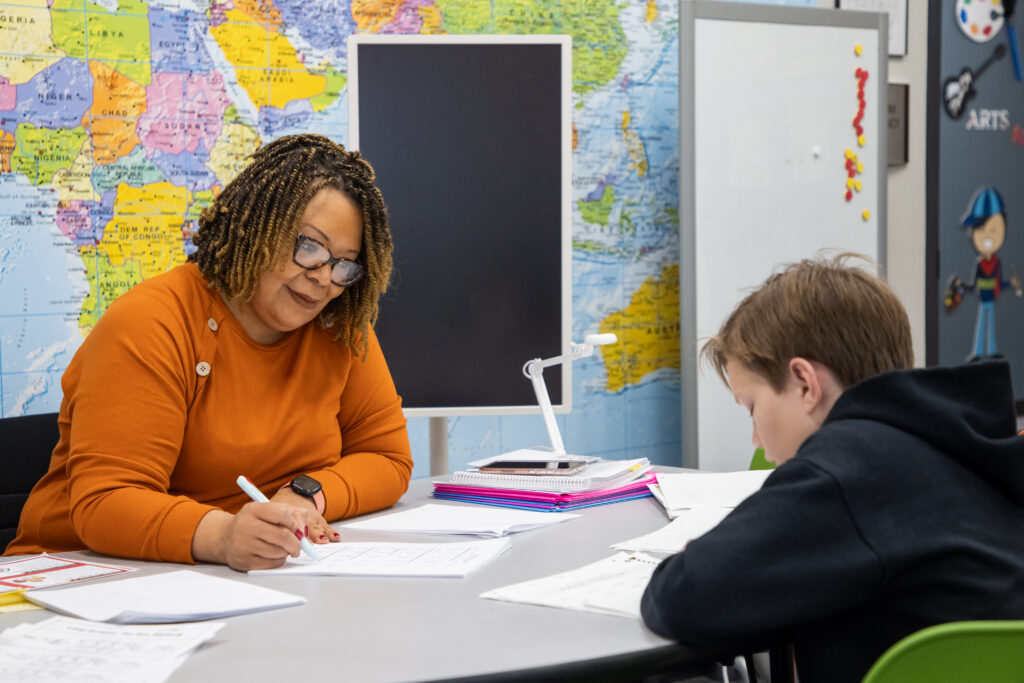 A dyslexic student works with a Roberts Academy faculty member at a large table in a classroom. 